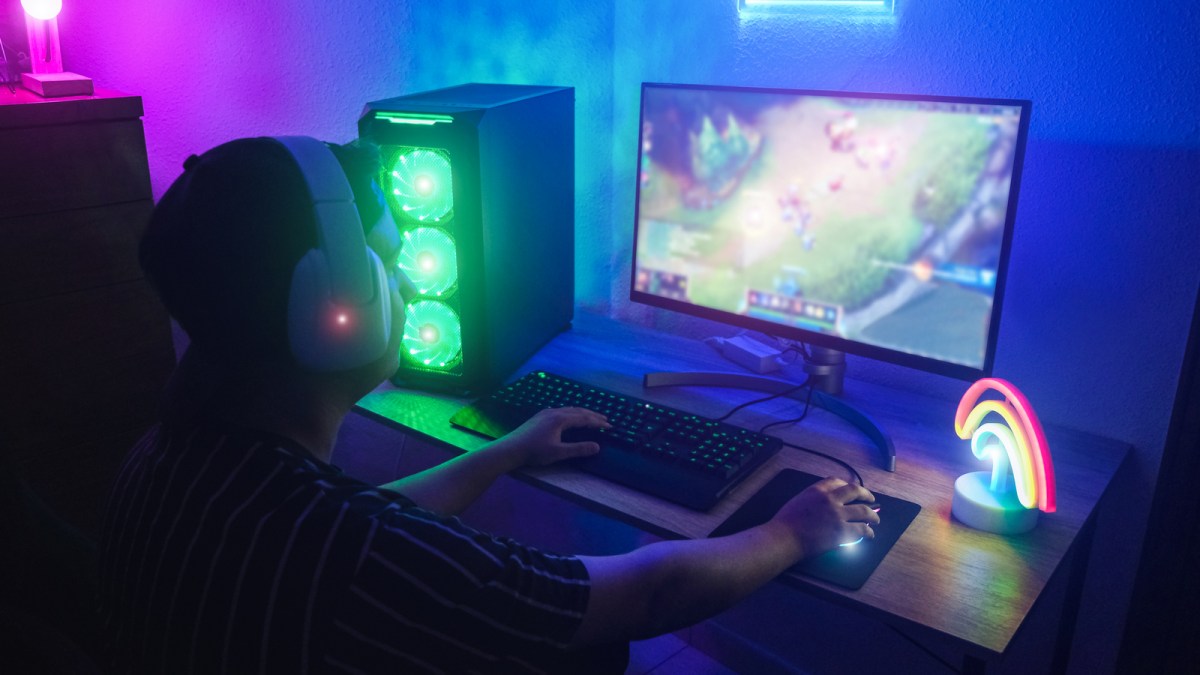 Young gamer playing online with neon lights in background - Male guy having fun gaming and streaming in internet with pc - Technology millennial trends, entertainment concept - Focus on right hand