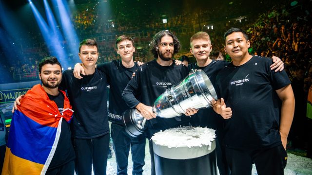 Jame from Outsiders holding the IEM Rio Major trophy on stage with his teammates standing behind him.