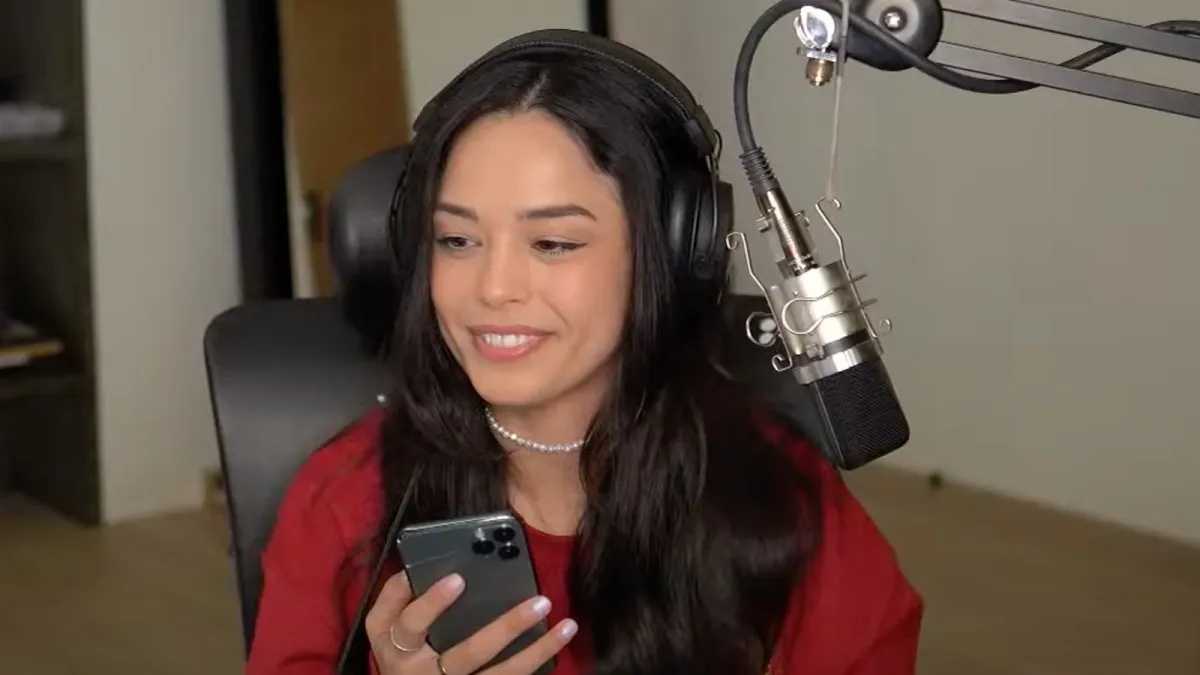 Valkyrae sits in front of a microphone while holding a phone.