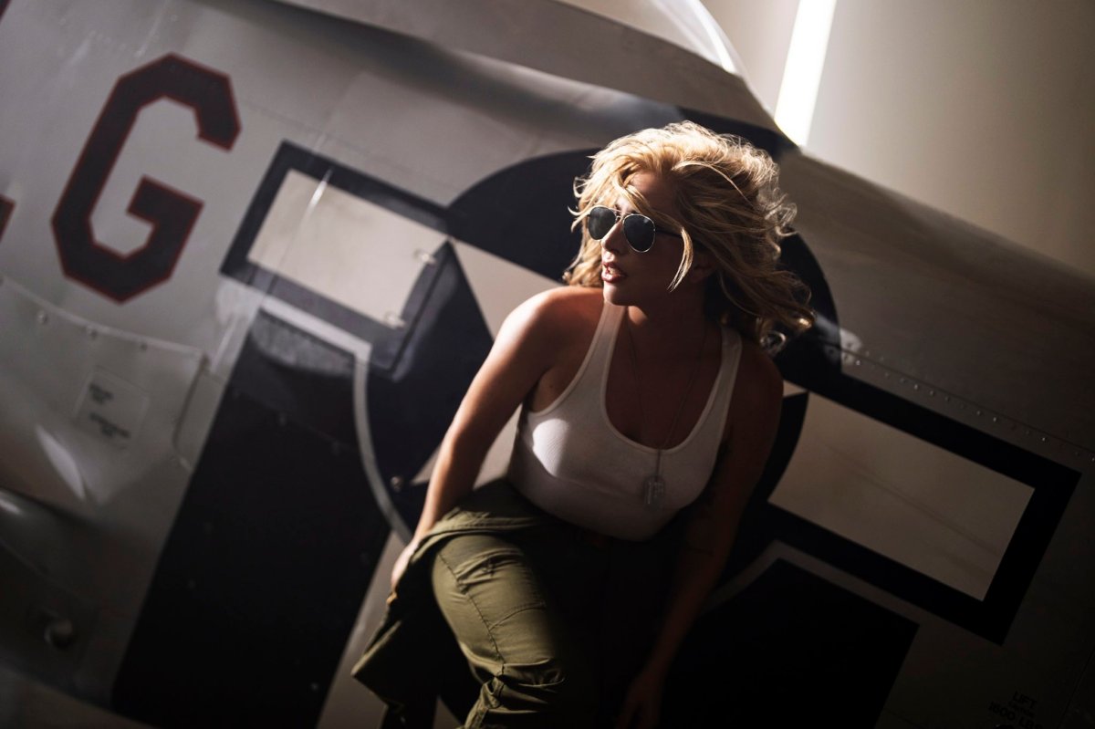 An image of Lady Gaga crouching in front of a fighter jet