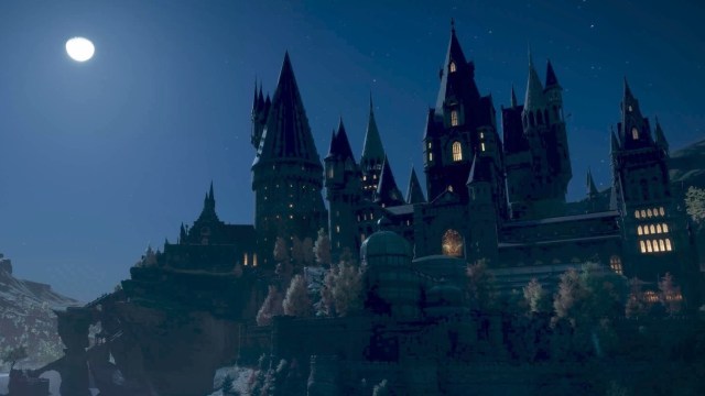 The Hogwarts castle with many spires rising into the night sky below a full moon in Hogwarts Legacy.