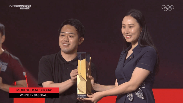 Mori Shoma poses with his Olympic Esports Series trophy and the trophy presenter after winning the finals.