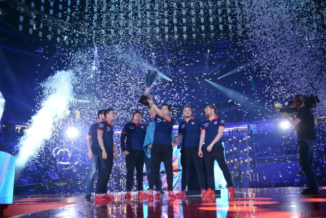 HObbit from Gambit holding the PGL Major Krakow trophy surrounded by his teammates while confetti is falling on the stage.