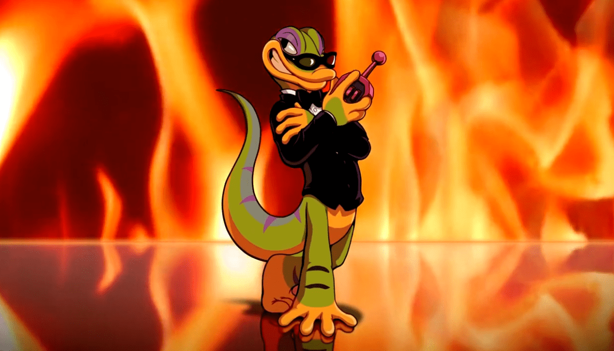 Gex, an animated bipedal green lizard with purple stripes, stands wearing a black long sleeve suit in front of a background of flames. He smiles and holds a remote of some kind.