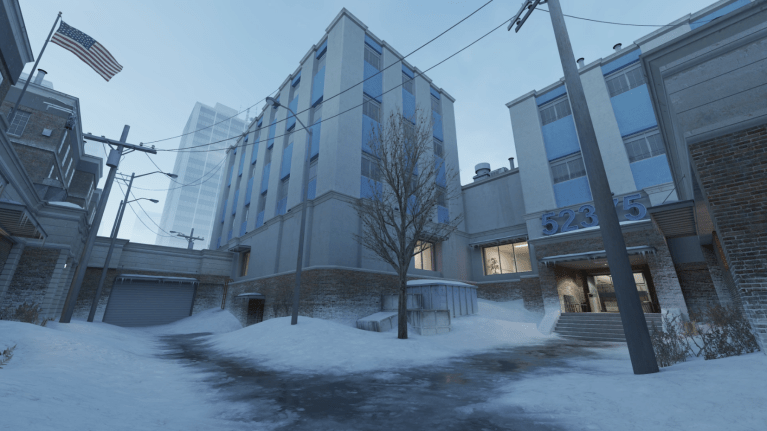 Official image of CS:GO hostage rescue map Office. It has plenty of snow, buildings, and one U.S. flag.