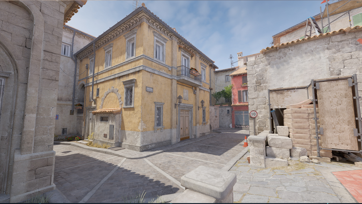 A cobblestone street and a yellow building, marking the location of the B bombsite on Inferno in CS2.