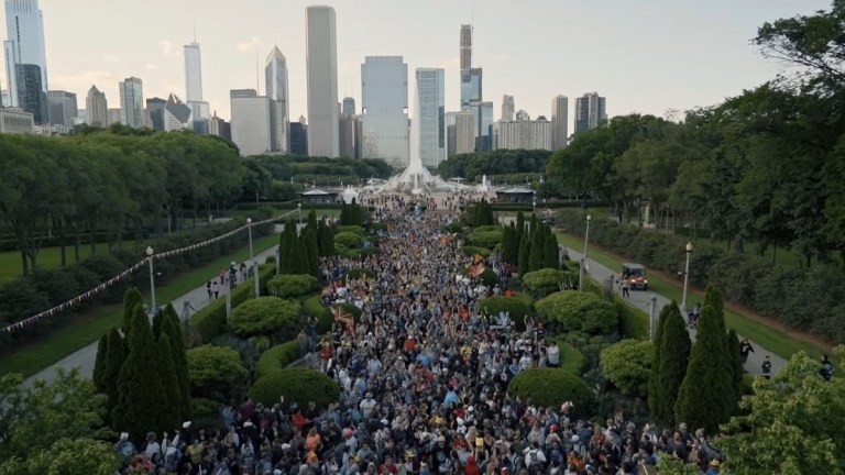 Players congregate in a large park with a fountain in front of the Chicago skyline, playing Pokemon Go.