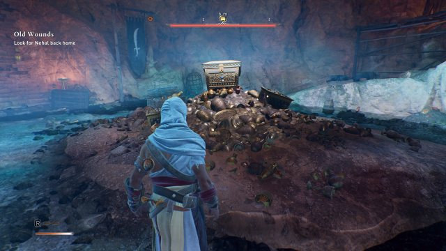 A character stands staring at a Gear Chest on top of a pile of treasures in a cave in Assassin's Creed Mirage.