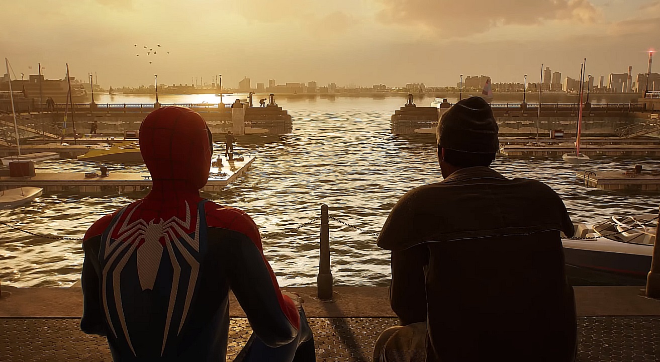 There is a shot of Spider-Man sitting with a man at the docks. It is sunset and there are people walking on the docks. 