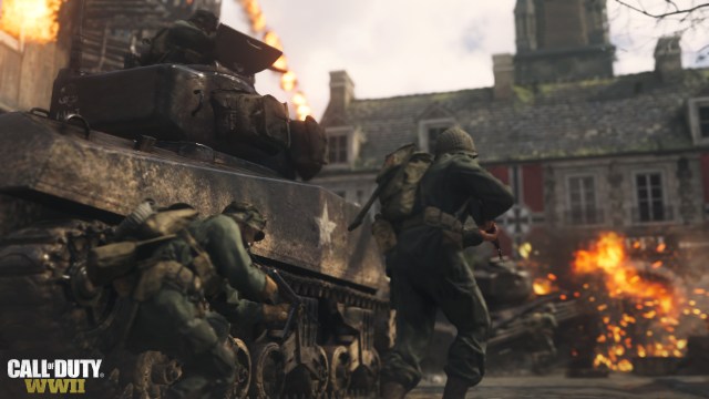 Two soldiers in World War II, hiding beside a tank as a vehicle explodes in front of them. 