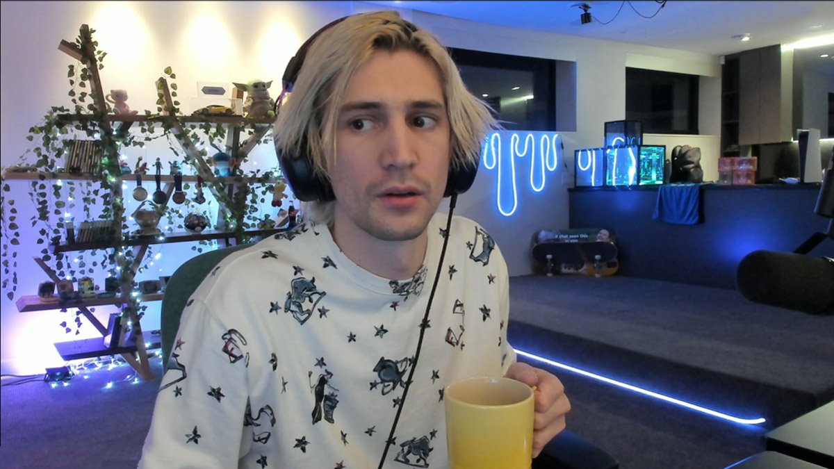 XQc, a streamer, sits holding a mug of coffee at his desk.