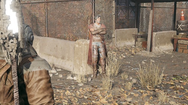 A rugged-looking man in a leather trenchcoat leans against a fence in Remnant 2.