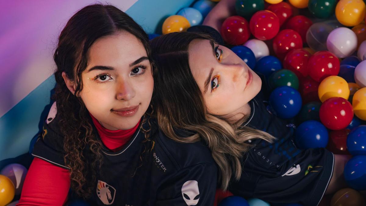 Two Team Liquid models sit in a ball pit wearing Liquid's Pride jerseys.