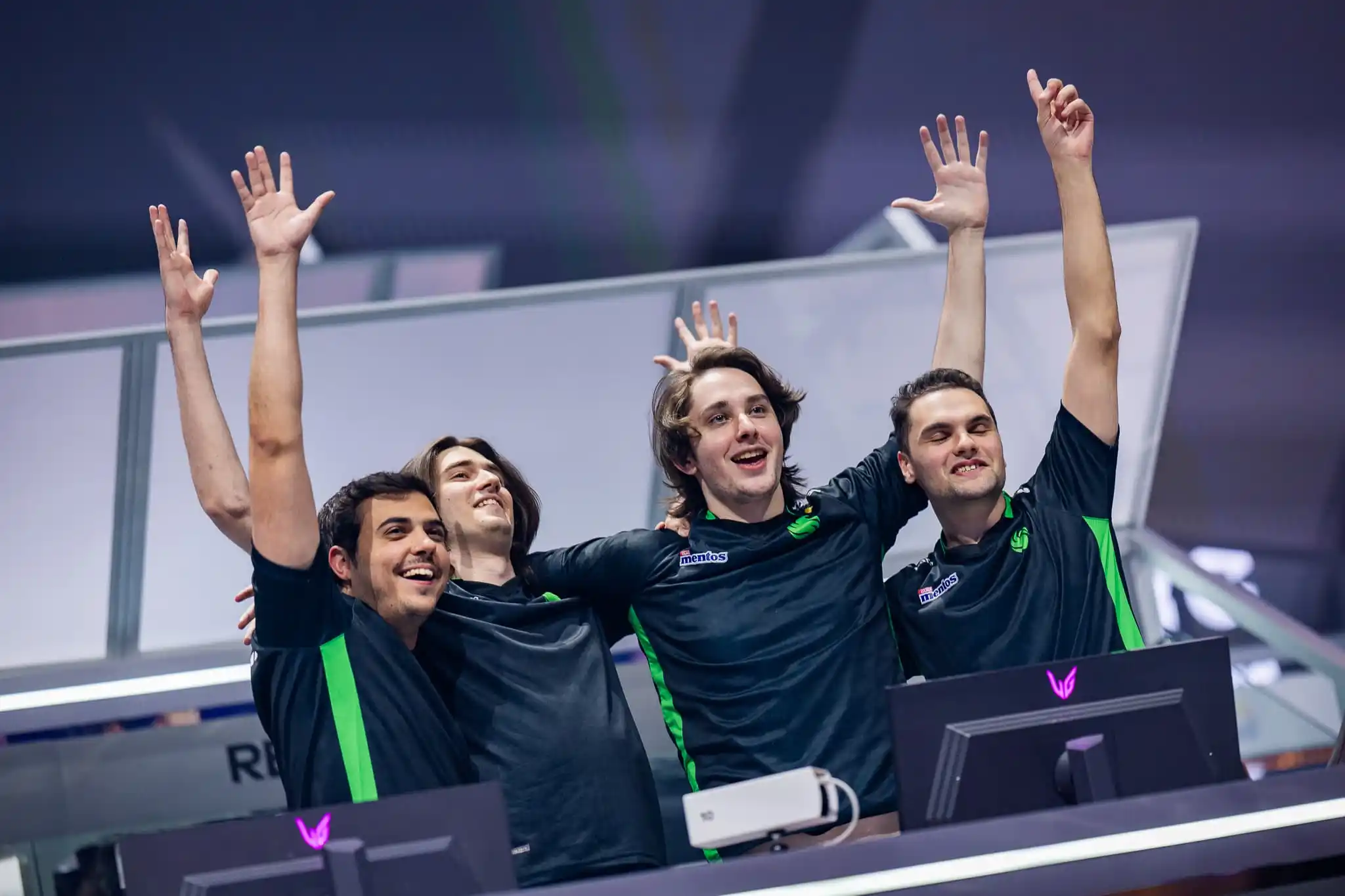 ImperialHal, Zer0, Genburten, and team coach ZZ from Team Falcons celebrate with their arms up toward the crowd.