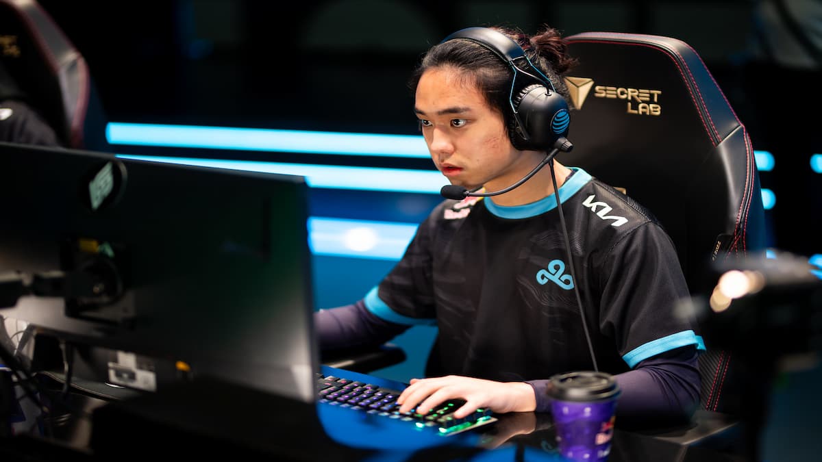 A man wearing a headset and black jersey, sitting in a chair and looking at a monitor in front of him.