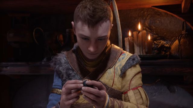 A red-haired young man wearing a Nordic fur tunic examines a marble. Image of Atreus from God of War Ragnarok