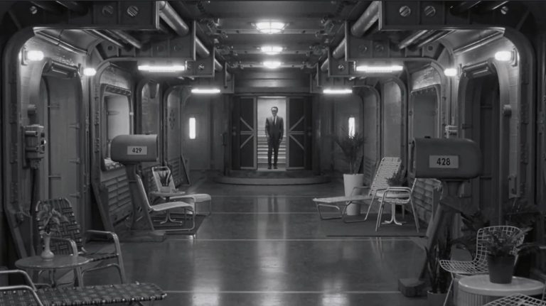 A man exits an elevator in an underground bunker lined with old-fashioned mailboxes and industrial lights.