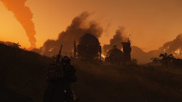 A Helldiver stands in a grassy field as the sun sets behind an ICBM pumping silo in Helldivers 2.