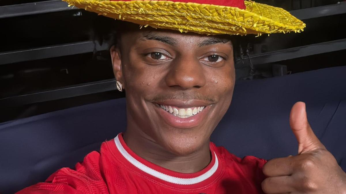 IShowSpeed smiles broadly with his thumb raised while wearing a red football jersey and a straw hat designed like Luffy's from One Piece.