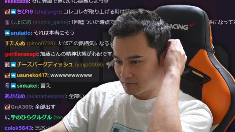 Junichi Kato holds the back of his head while sitting on his gaming chair. Behind him appears a super-sized version of his Twitch chat where fans are praising him.