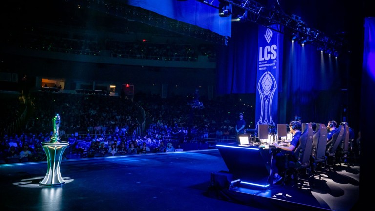 The LCS trophy sits on a plinth to the left of a team playing on-stage at the LCS Summer 2024 playoffs.