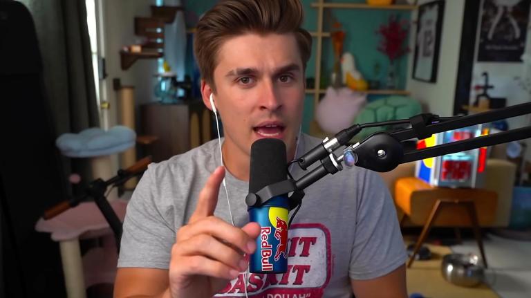 Ludwig speaks to his YouTUbe audience directly down the camera with one finger raised. He's speaking into a Red Bull microphone and is in a streaming-designed room with lots of logos and memorabilia.