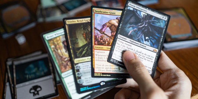 Someone's hand holding several different physical Magic the Gathering cards.