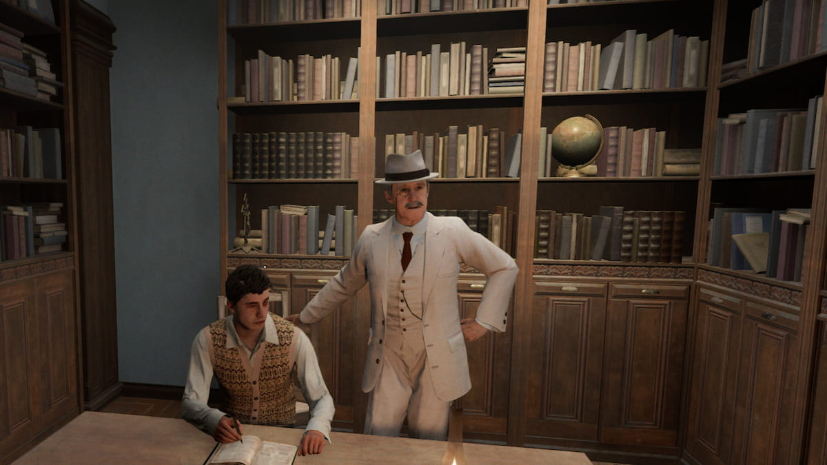 A man man in a white three piece suit and hat stands behind another man sitting down. Both are in front of a shelf full of books.