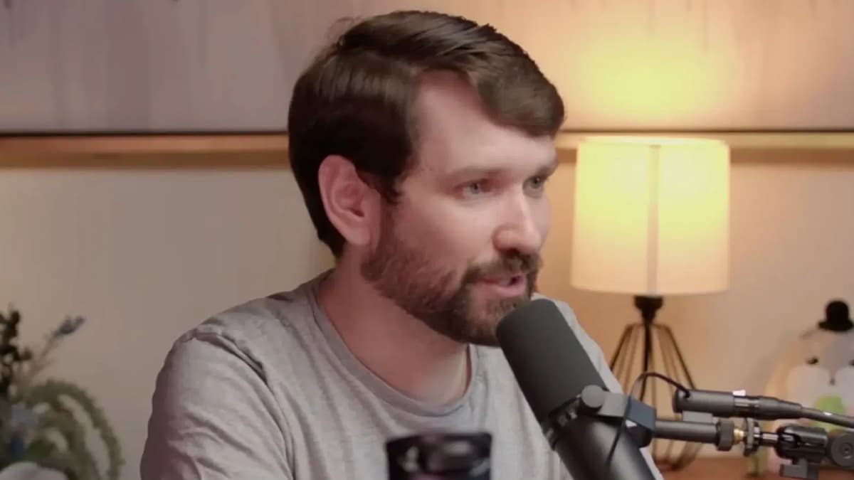 Streamer Destiny sitting at a table and speaking into a microphone with a strong yellow lamplight behind him.