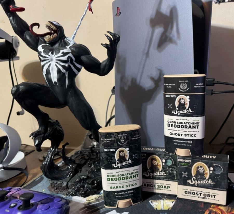 A stack of Squatch deodorant sitting next to a PS5 and a Venom statue.